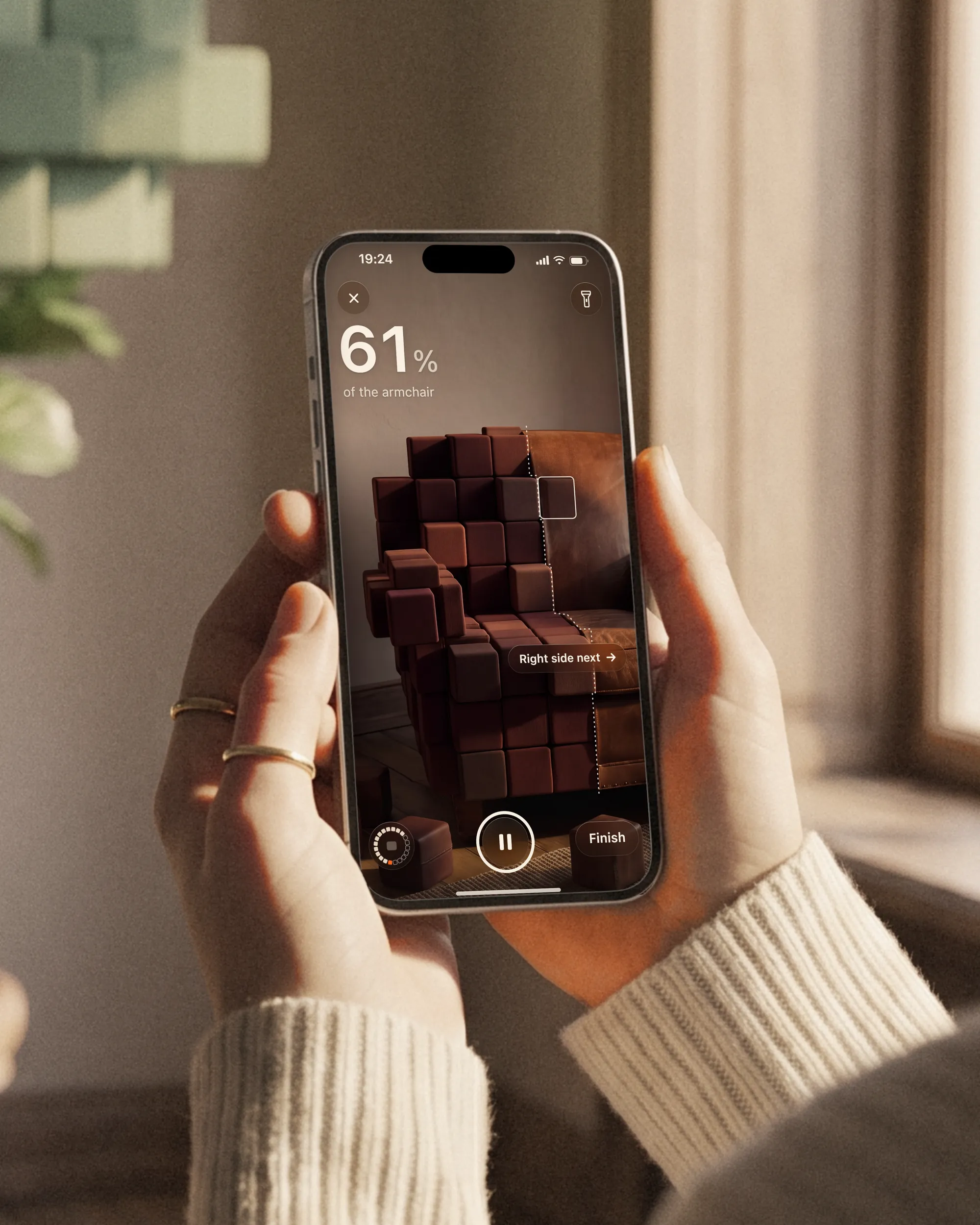 A hand holds an iPhone by a sunny window while Kubo shows the leather armchair part turned into cubes