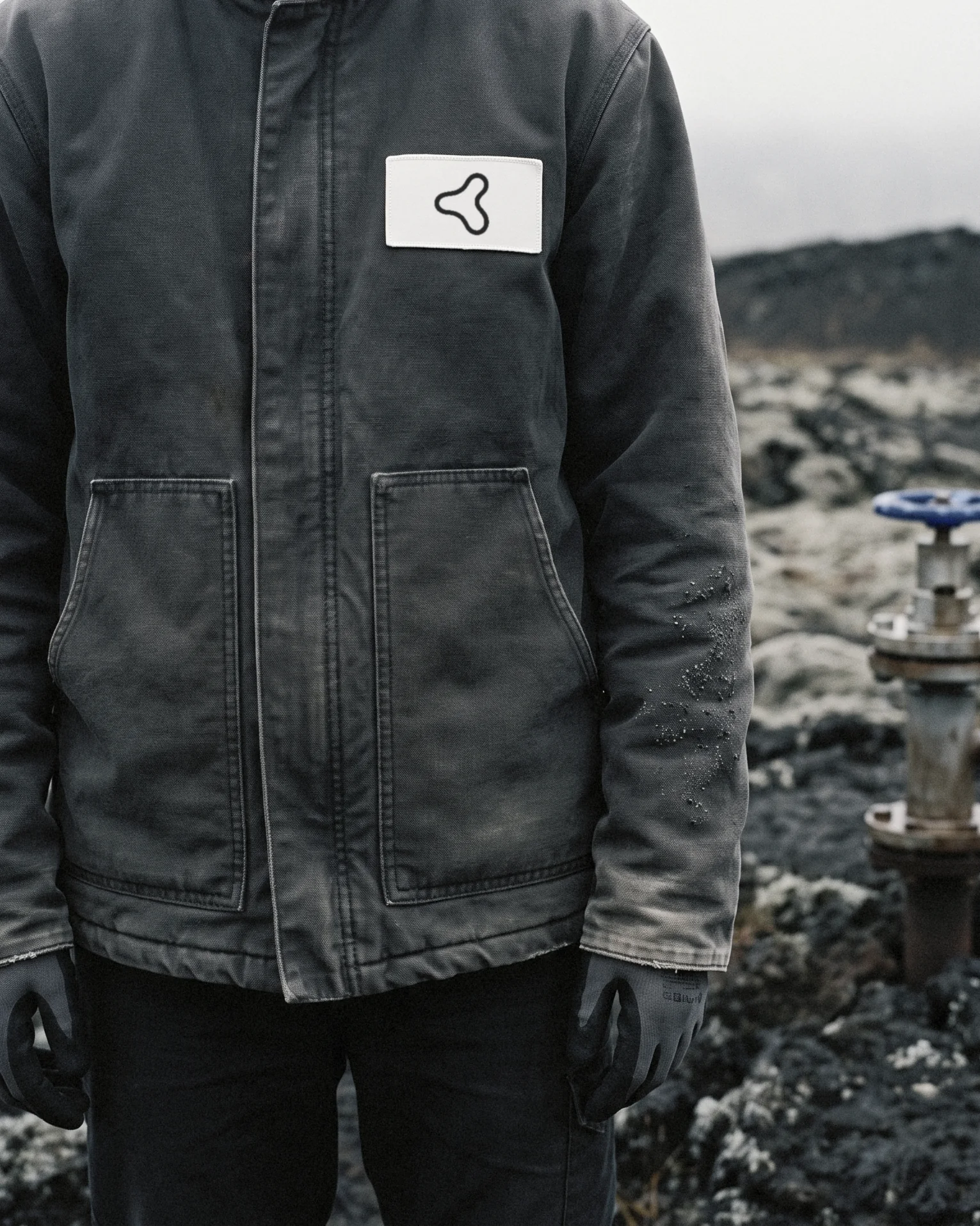 A field technician's work jacket with the Membrane mark on a woven chest patch, a wellhead behind
