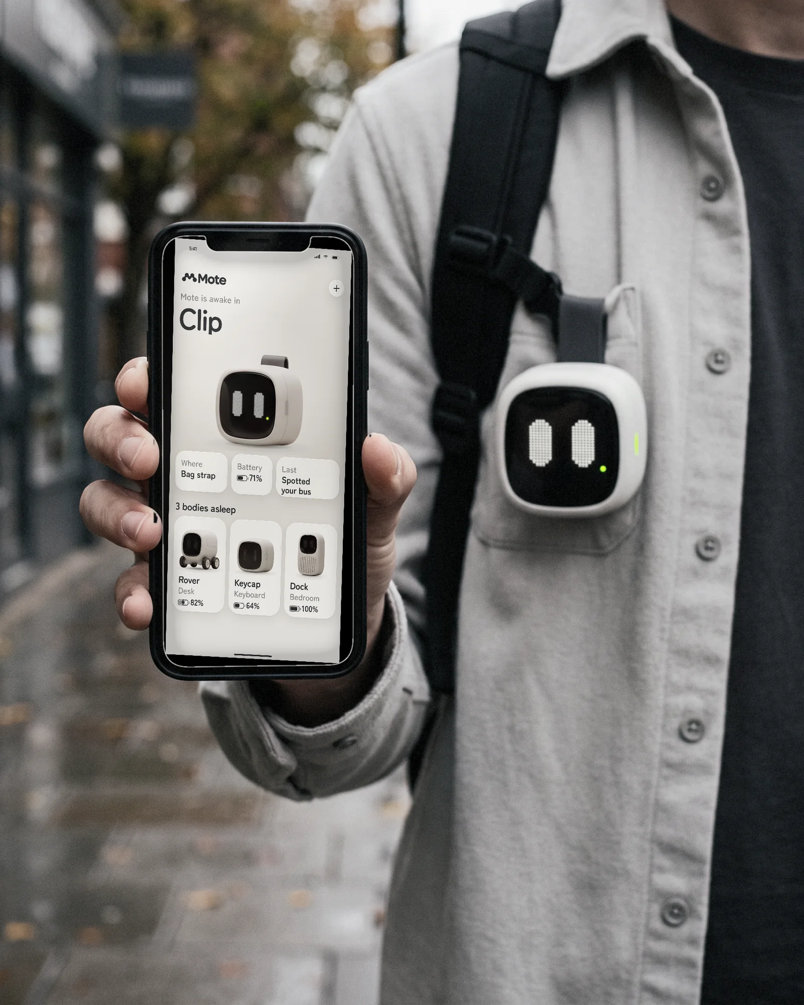 A hand holds the Mote app on a wet street, the clip camera awake on the strap